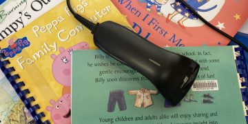 A library bar code scanner lies on a pile of brightly coloured ClearVision children's picture books.
