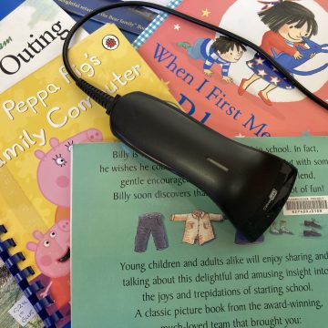 A library bar code scanner lies on a pile of brightly coloured ClearVision children's picture books.