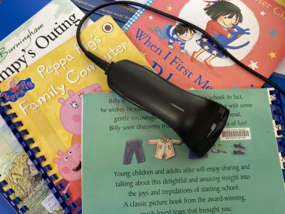 A library bar code scanner lies on a pile of brightly coloured ClearVision children's picture books.